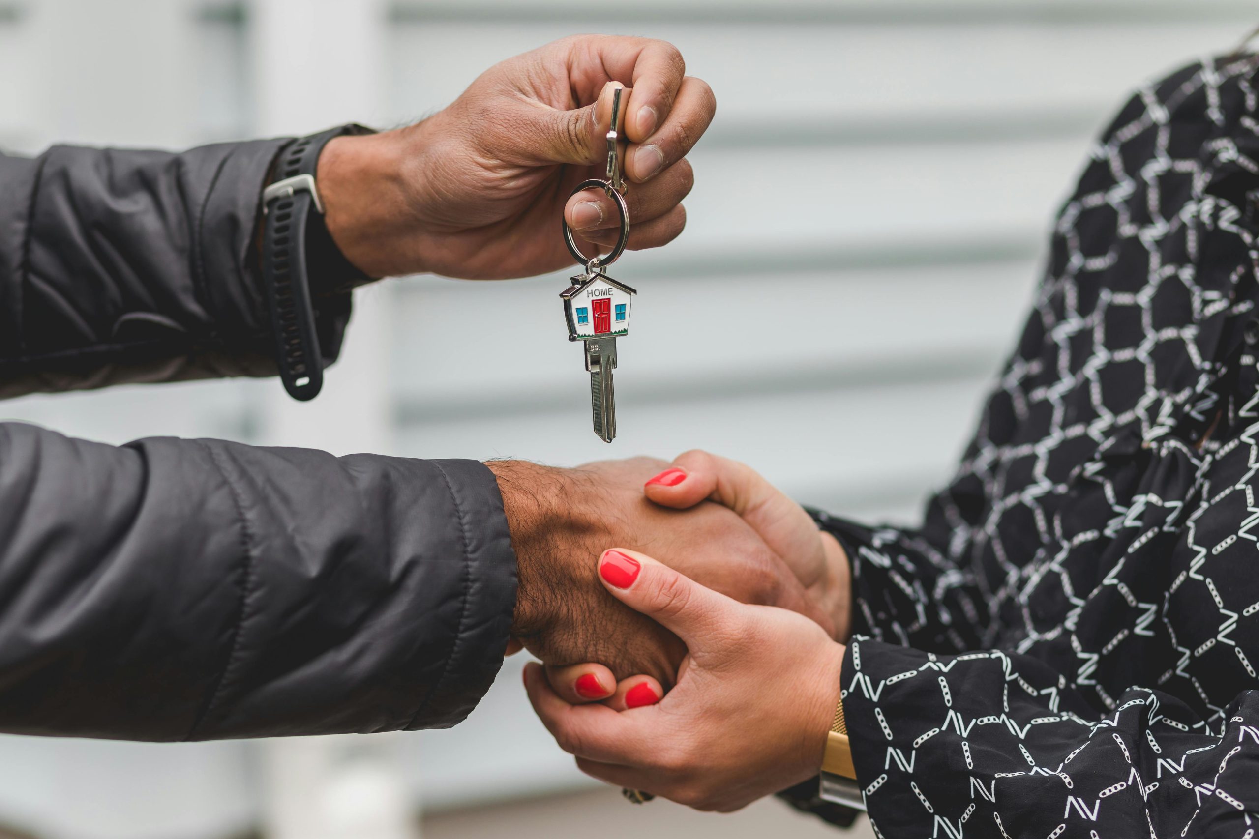 Real estate agent holding clients right hand while buyer holds key to new home in left hand.
